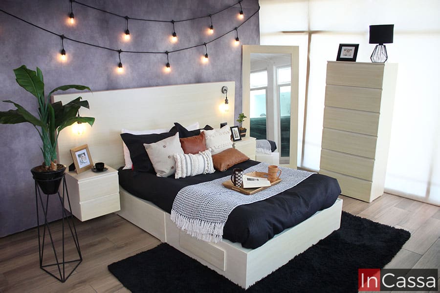 Recámara Matrimonial en color paja completa instalada en una habitación con pared gris y piso de madera. Además de la cabecera con lamparas minimalistas y los dos buroes, la recámara cuenta con espejo y cajonera.