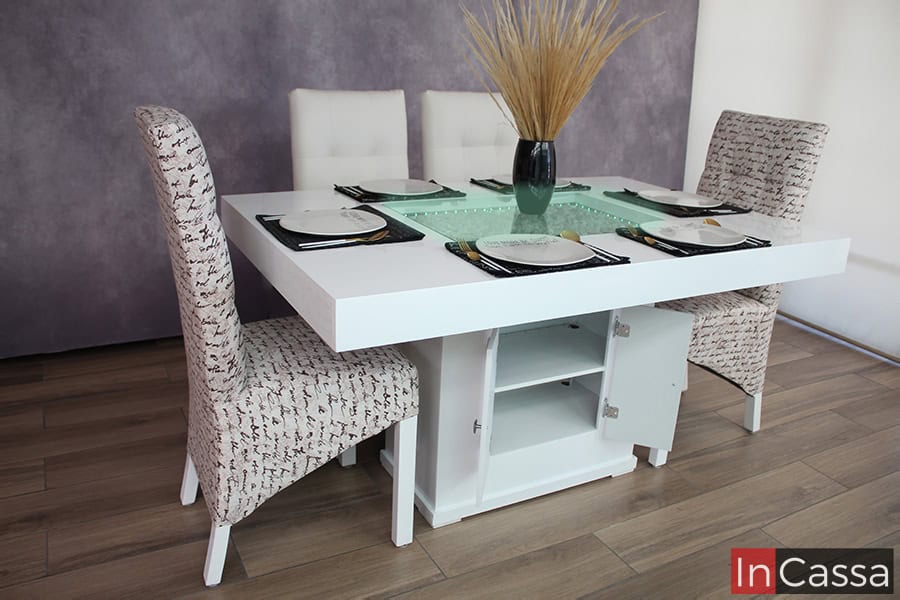 La imagen muestra el comedor para 6 personas sin dos de sus sillas, esto con el fin de dejar a la vista los compartimentos integrados al pedestal, los cuales están separados por un entrepaño horizontal y cubiertos por dos puertas.