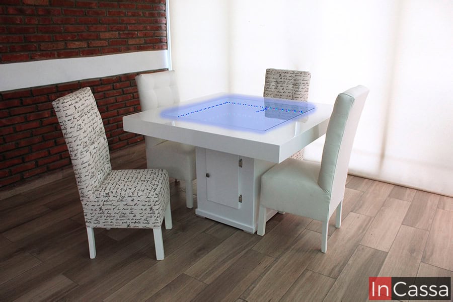 En esta foto se muestra el comedor en su presentación para 4 personas, esta vez con la iluminación LED de su arenero en un tono azulado. Gracias a la posición de las sillas queda visible el compartimento integrado a su pedestal con puerta.