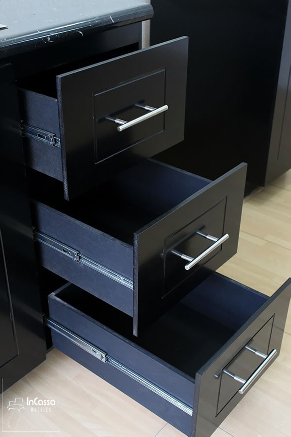 La foto muestra los cajones de la cocina, los cuales son muy amplios y profundos, con rieles metálicos de alta resistencia que aseguran un deslizamiento suave y duradero. Los tiradores modernos en acabado metálico complementan el elegante diseño negro mate, ofreciendo tanto funcionalidad como estilo en el almacenamiento de utensilios y accesorios de cocina.