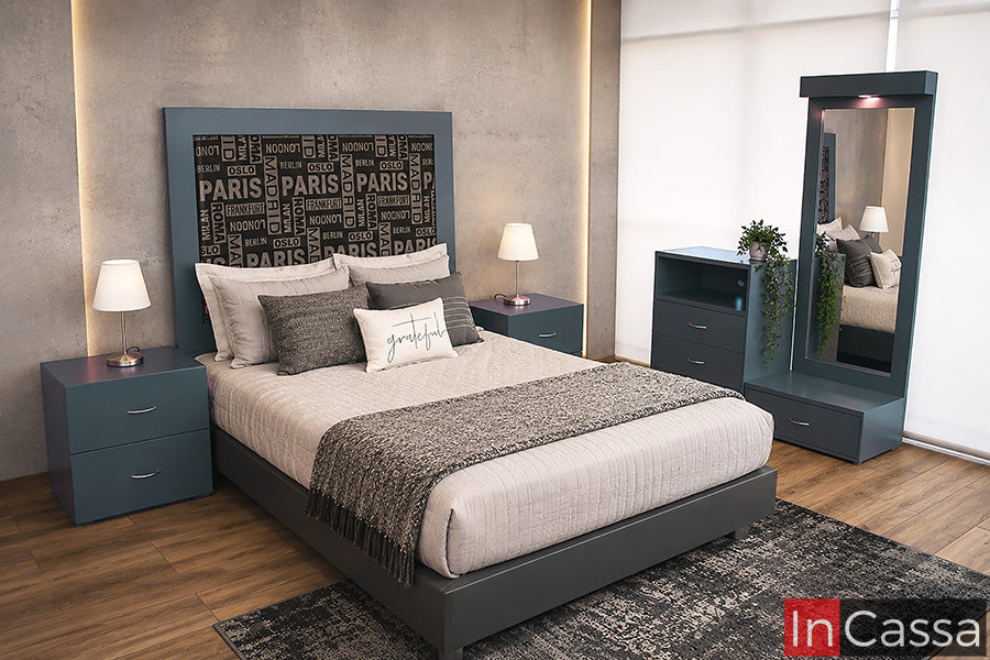 Se observa la Recámara Modelo GUINEA, en color gris oxford, con una cabecera que integra un detalle tapizado en lino estilo ciudades. El conjunto se complementa con burós, cómoda y tocador con espejo, logrando un diseño moderno, urbano y funcional.