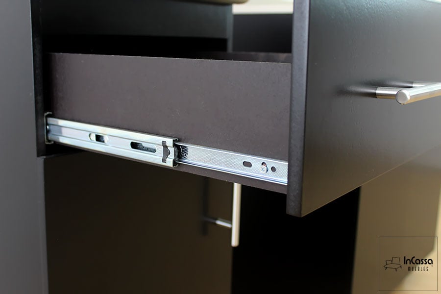 La toma presenta un acercamiento al sistema de corredera metálica de extensión incorporado en los cajones de la cocina HAMPTON para estufa. Se observa el acabado chocolate mate del mueble y la jaladera cilíndrica de acero inoxidable, que aporta funcionalidad y estilo moderno.