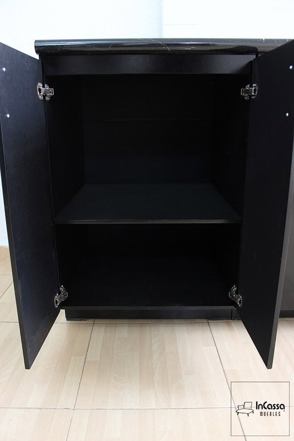 La imagen muestra un gabinete inferior en acabado negro con doble puerta y jaladeras metálicas. Su interior espacioso cuenta con un estante fijo que permite organizar utensilios, ollas o despensa. Las bisagras reforzadas garantizan resistencia y un cierre seguro, optimizando el almacenamiento en la cocina.