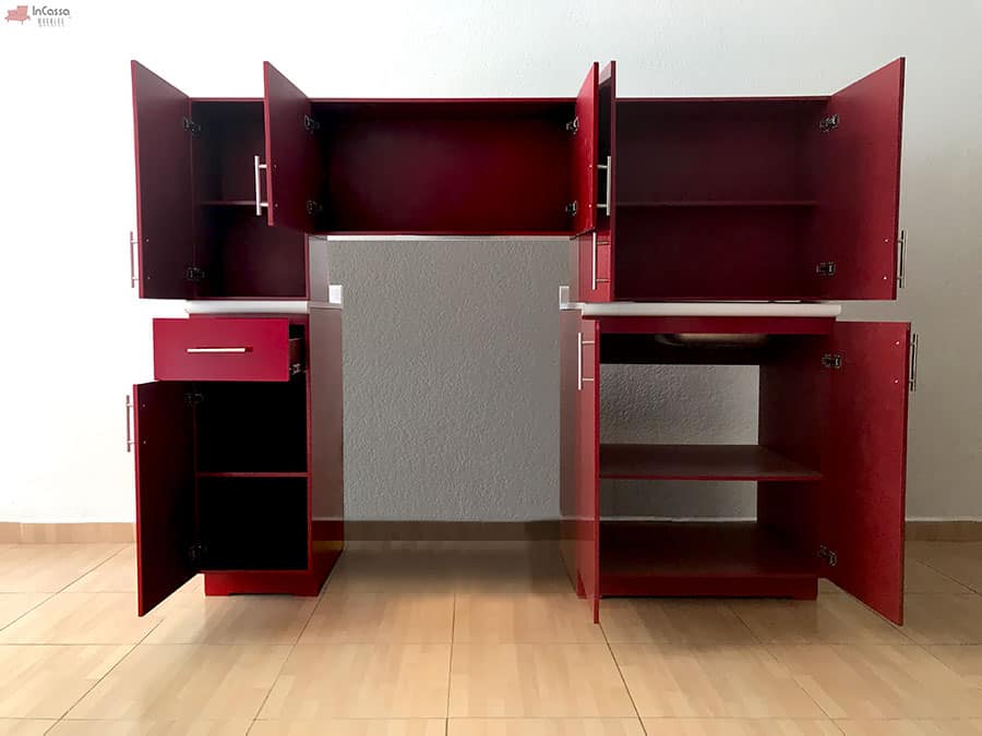 La imagen presenta una toma completa de la Cocina HAMPTON para estufa con todos sus módulos abiertos, revelando compartimentos amplios, repisas interiores funcionales y un cajón lateral con correderas metálicas, todo en elegante tono rojo quemado con cubiertas de formaica blanco fresh.