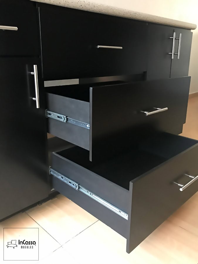 Primer plano de los cajones de la cocina, destacando su construcción robusta y su diseño funcional en acabado chocolate mate completo. Los rieles metálicos garantizan un movimiento suave y duradero. Mientras que las jaladeras de barra metálica aportan un toque de elegancia y modernidad, complementando la cubierta de formaica.