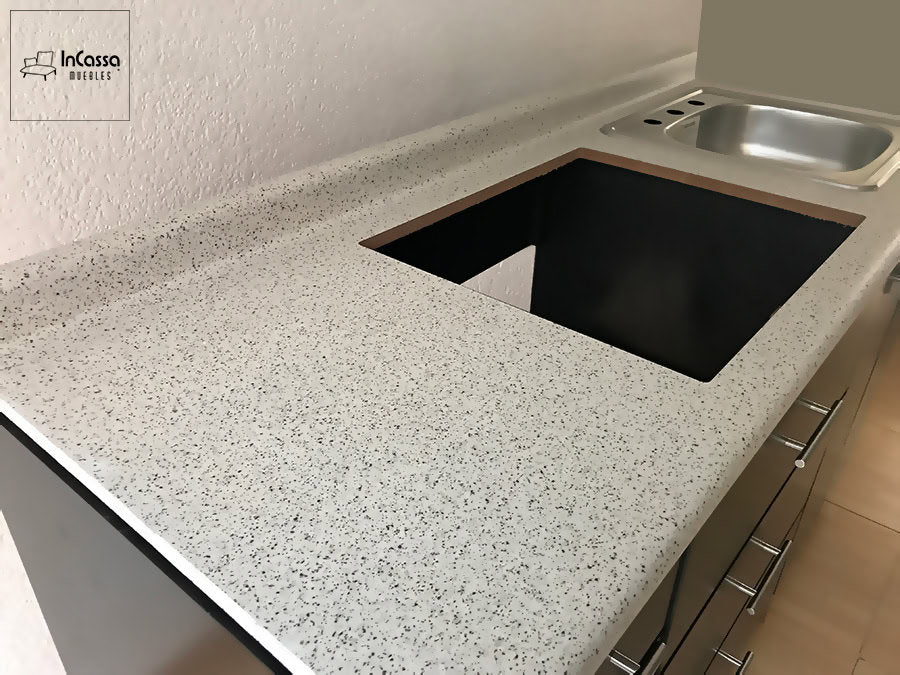 Cubierta de formaica con acabado sal y pimienta en la cocina, destacando un espacio preparado para la instalación de una parrilla empotrable. El diseño ofrece una superficie amplia y resistente, ideal para preparar alimentos. A la derecha, se observa la tarja de acero inoxidable, completando una configuración moderna y funcional.