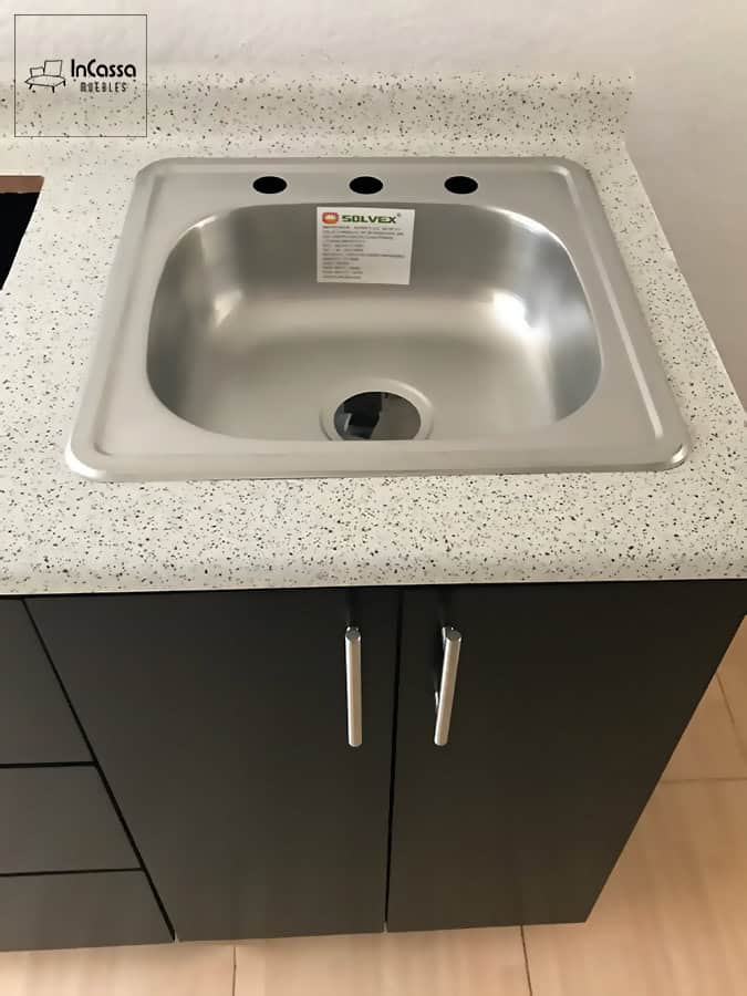 Una toma del área de tarja en la cocina, equipada con una tarja de acero inoxidable encastrada en una cubierta de formaica en estilo sal y pimienta. Los gabinetes inferiores, con jaladeras de barra metálica, proporcionan un almacenamiento adicional y fácil acceso. Diseño moderno y funcional, ideal para cualquier hogar.