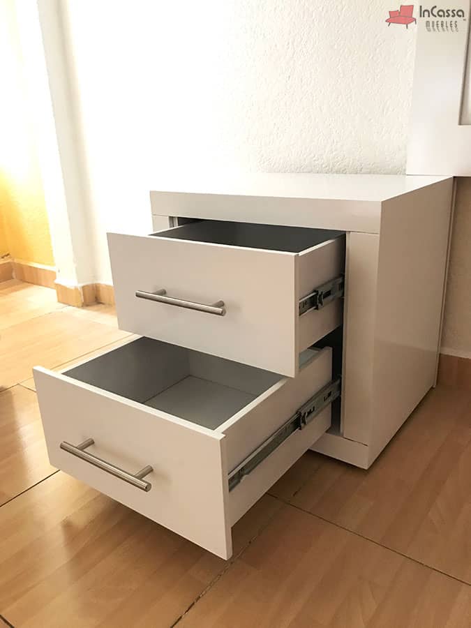 Una toma en ángulo muestra el buró blanco moderno con dos cajones abiertos, revelando su interior amplio y rieles metálicos de extensión. El diseño de líneas rectas y jaladeras tipo barra lo hacen funcional y elegante para cualquier recámara.