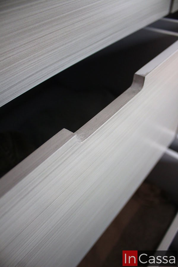 Imagen del borde superior de uno de los cajones, en el que se puede notar un pequeño espacio que cumple con la función de jaladera para el compartimento. Además la cercanía de la toma también permite apreciar mejor el acabado gris cenizo claro de la cajonera.