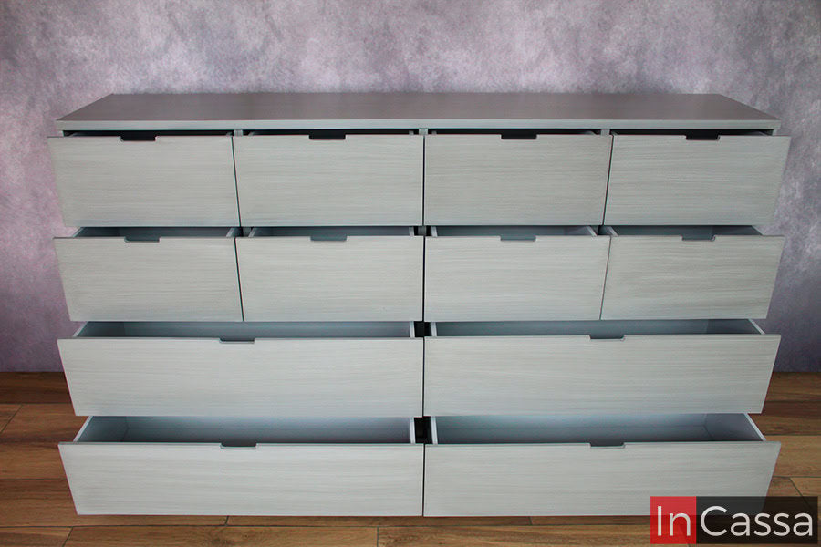 Una foto frontal de la cómoda - cajonera desde una toma superior, en la que se muestra el mueble de color gris completo con todos sus cajones semi abiertos, dejando a la vista parte de su interior.