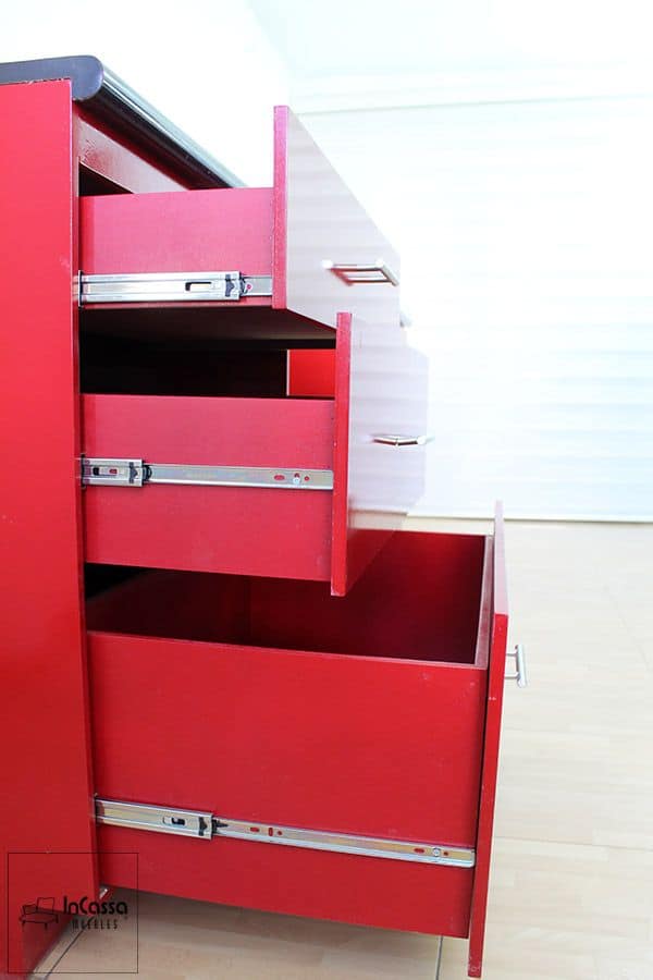 La foto destaca tres cajones en acabado rojo quemado brillante, equipados con correderas de extensión metálicas que permiten una apertura suave y total. El diseño robusto y funcional maximiza el almacenamiento en cocinas modernas.