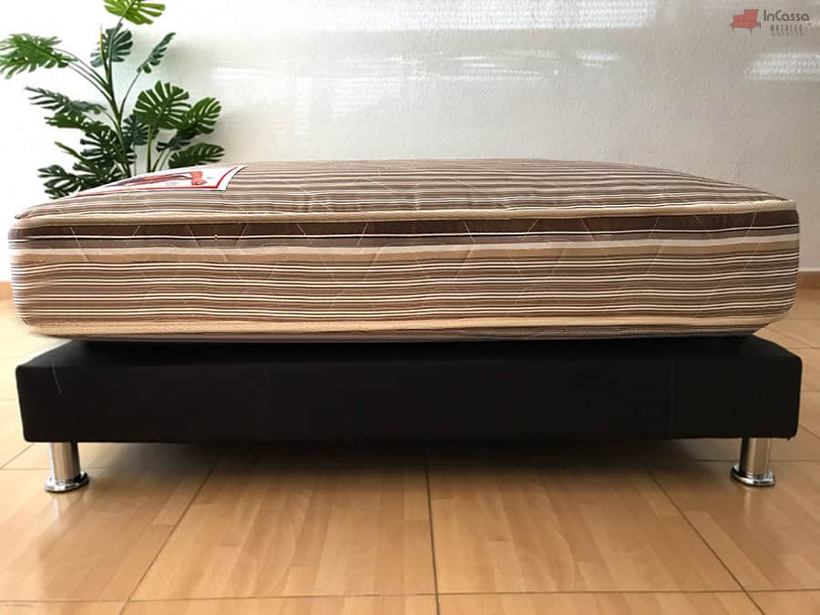 Se nos presenta una toma frontal del colchón hotelero, en la que gracias a la base de cama, queda mucho más visible la densidad del acolchonado cuyo tapiz tiene un patrón rayado.