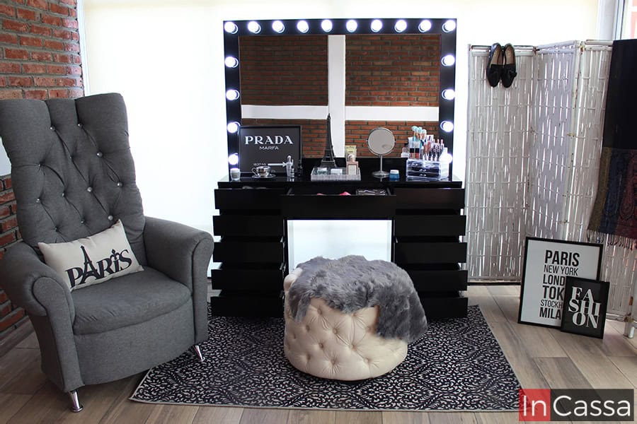 Tocador negro completo con espejo de 18 focos, presentado en una habitación con ventana de pantalla completa y varios artículos decorativos. El tocador cuenta con 5 cajones de cada lado y uno central.