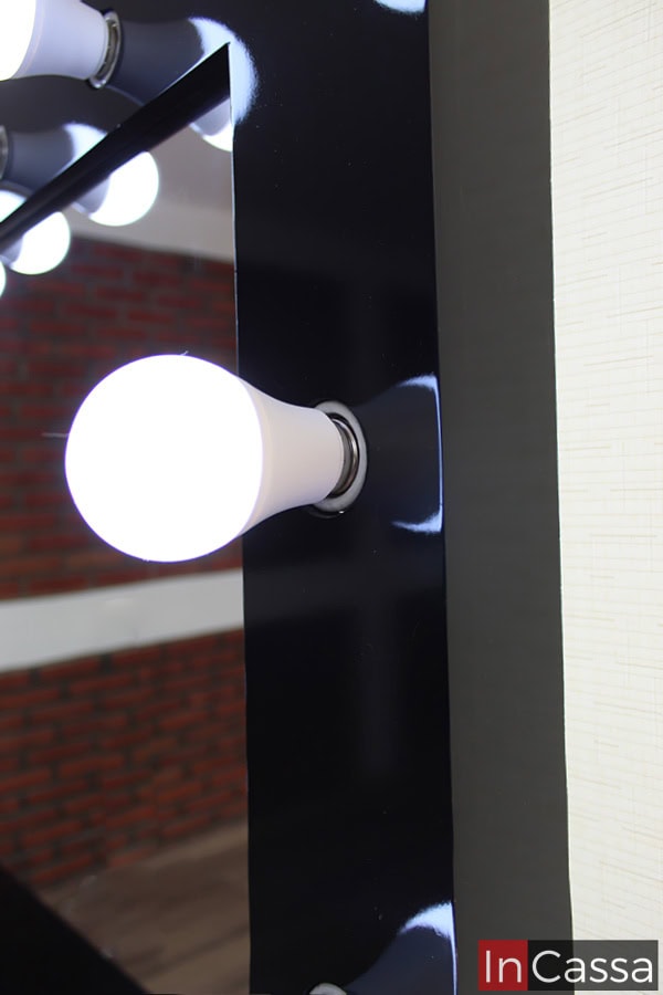 La foto nos da una mirada cercana a uno de los 18 focos integrados al espejo del tocador, dejándonos ver que se trata de un foco led de luz pálida. También se puede apreciar más a detalle el acabado negro en el marco del espejo.