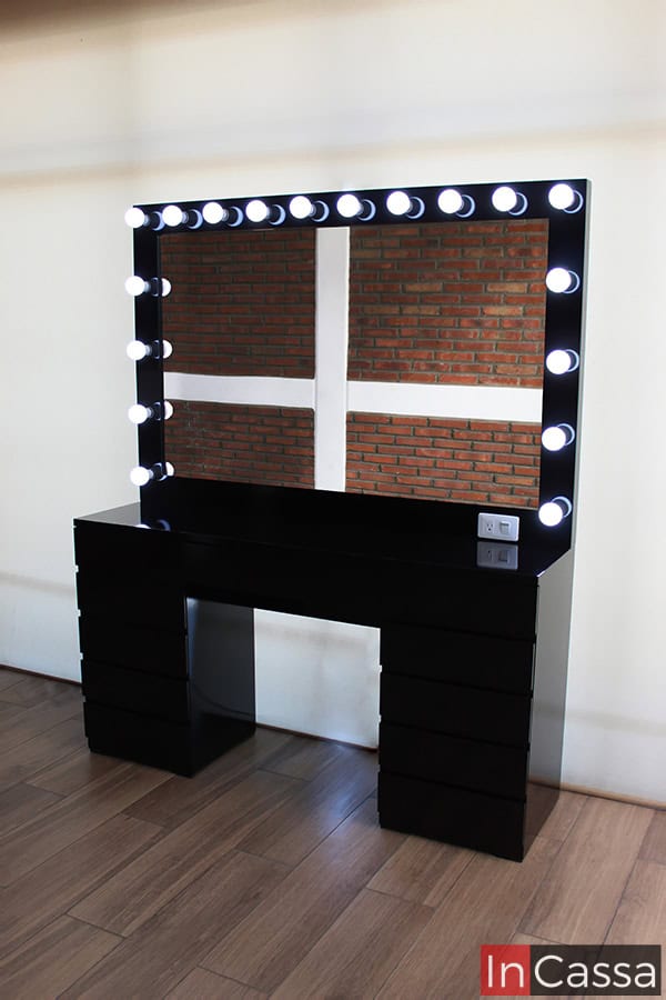 Una toma lateral del escritorio chocolate, en la que podemos apreciar más a detalle la cubierta y la propia estructura del mueble, el cual presenta un acabado negro brillante en su totalidad. El ángulo favorece igualmente al espejo, dando una mejor vista de sus dimensiones así como de los 18 focos incluidos en el marco del mismo.