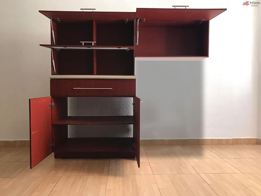 La foto presenta la cocina integral abierta, mostrando sus espacios de almacenamiento, dejando a la vista su acabado maple oscuro completo. Los gabinetes superiores cuentan con divisiones internas y puertas con pistones de soporte, ideales para organizar artículos de cocina. En la parte inferior, se observan puertas con bisagras de alta calidad y un cajón funcional para utensilios. Este diseño ofrece una distribución eficiente para maximizar la organización en cocinas compactas.