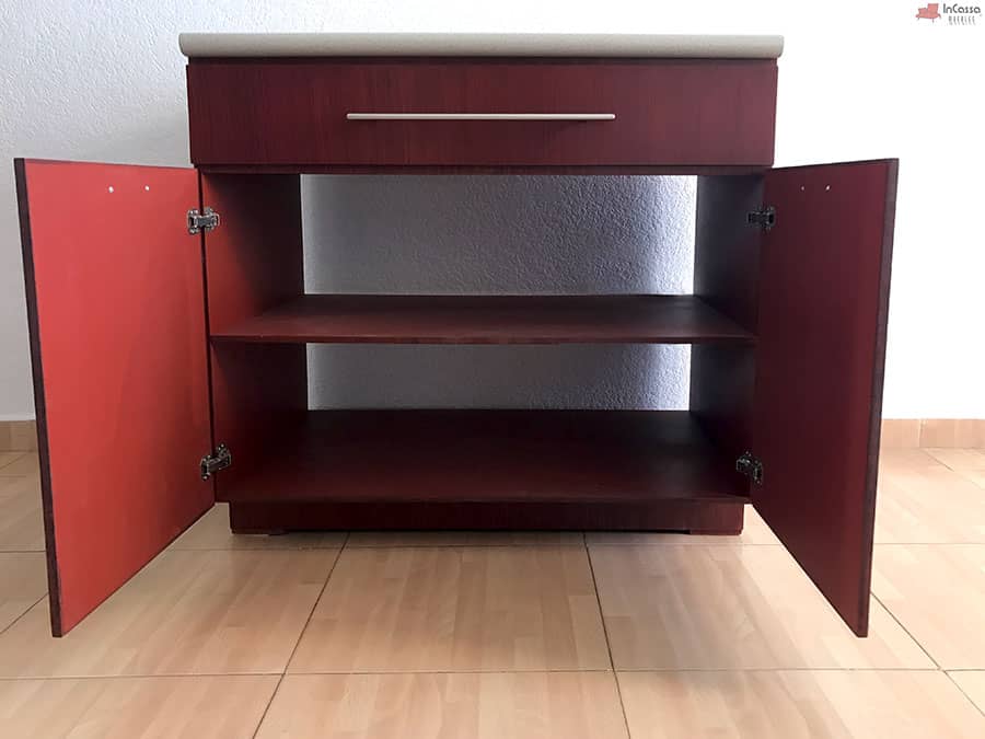 Una toma del espacio interior del módulo inferior en acabado maple oscuro. Este diseño incluye dos amplios estantes con puertas abatibles, ideales para almacenar utensilios y mantener la cocina organizada.