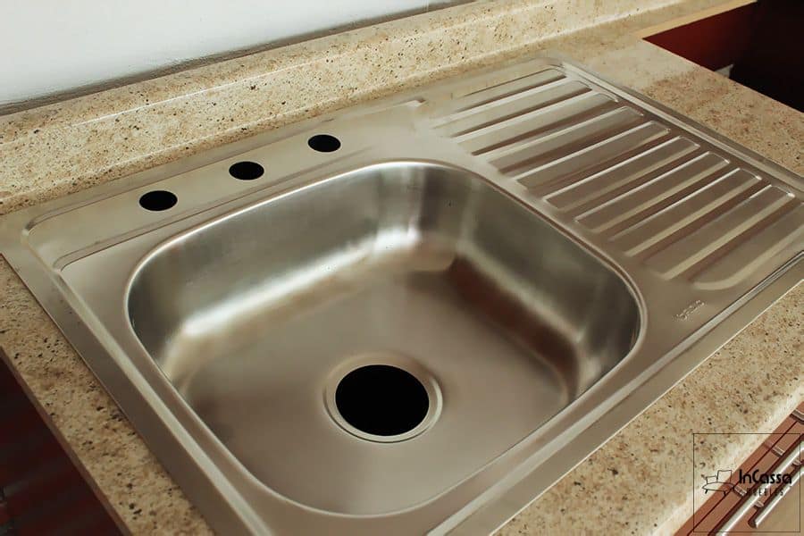 Una foto completa de la tarja incluida en la cocina, la cuál es de acero inoxidable con tina izquierda y escurridor en la parte derecha. La tarja esta instalada en una cubierta de formica con estilo ojo de pájaro.