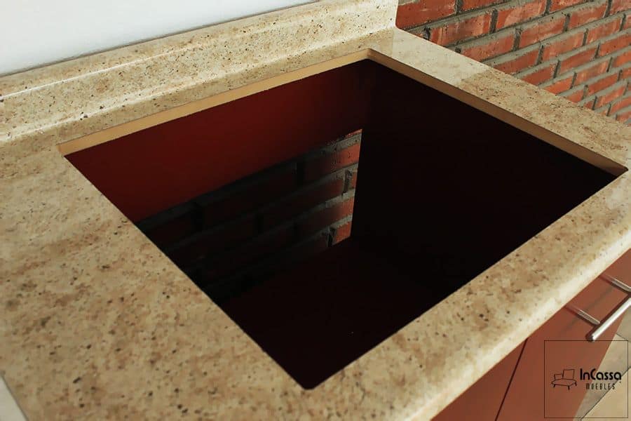 La imagen nos da una vista cercana del espacio para parrilla hecho en la cubierta de formica estilo ojo de pájaro. En el cuál podemos ver el interior del compartimento inferior, en el cuál se observa un espacio en la estructura para poder realizar la instalación de la parrilla empotrable con mayor facilidad.