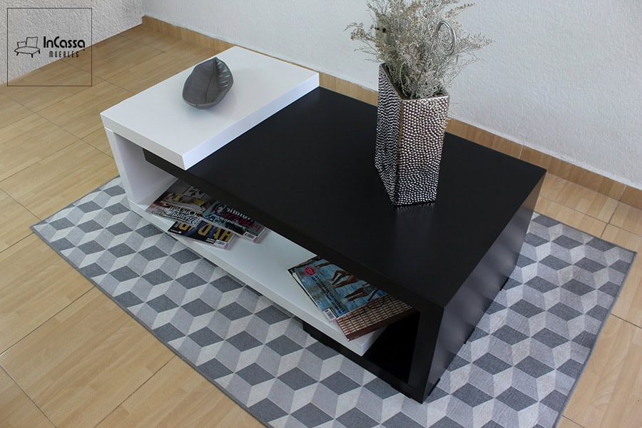 En esta imagen se aprecia la elegante combinación de colores y formas de la mesa de centro ISLANDIA, capturada desde una vista diagonal. La cubierta negra brillante contrasta perfectamente con el módulo blanco elevado, resaltando su estilo moderno y asimétrico.