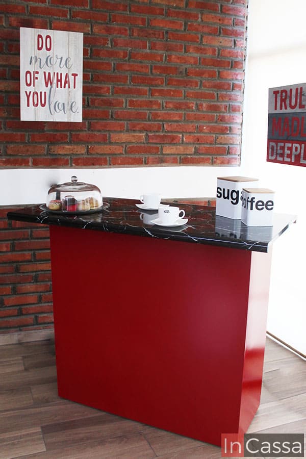 Toma lateral de la barra para cocina en la que podemos apreciar más a detalle parte de la estructura del mueble así como el acabado de su pintura roja, la cual presenta un tono brillante. También es posible comprobar la longitud de la cubierta de estilo mármol negro, además del grosor de la misma.