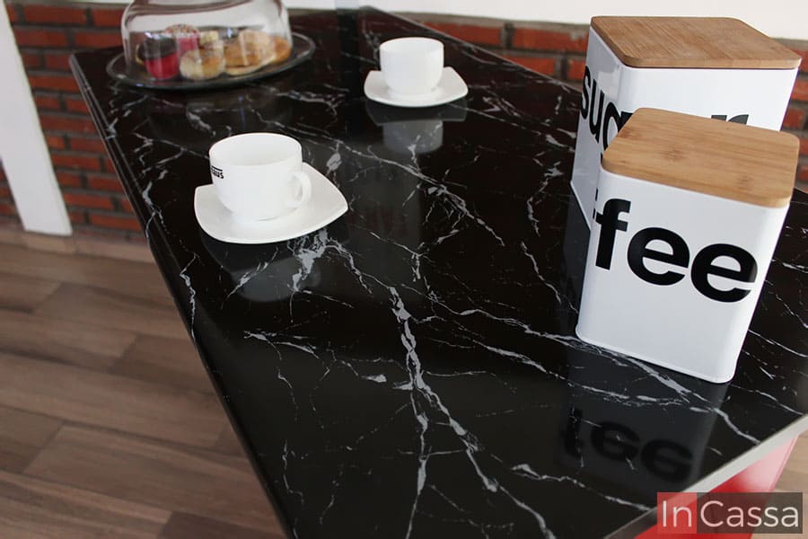 La toma nos muestra la longitud de la cubierta de formica de la barra, decorada con algunas vajillas de color blanco resaltando su estilo mármol negro.