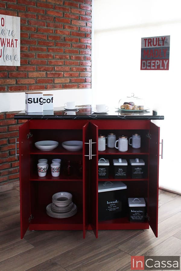 Una foto de la parte trasera de la barra con sus cuatro puertas abiertas, dejando visibles sus seis compartimentos interiores todos divididos por entrepaños horizontales. Cada espacio se presenta con distintos tipos de vajillas en su interior a fin de ejemplificar su profundidad y capacidad. Además es bastante noble que el mueble conserva el color rojo en la totalidad de sus interiores.