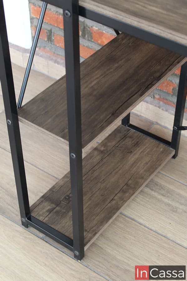 La imagen nos da una mirada cercana a las repisas laterales inferiores incorporadas al escritorio, las cuales son de MDF con un acabado laqueado; además también podemos comprobar el grosor de las barras metálicas que conforman la base del mueble.