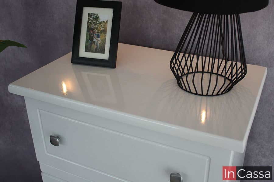 Una foto enfocada en la cubierta de la cajonera, la cuál resalta el acabado brillante de su pintura blanca. y en la que además tenemos una vista más cercana del cajón superior del mueble.