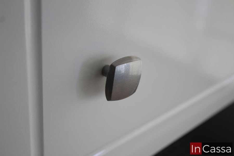 Una foto cercana de una de las jaladeras que puede verse en todos los compartimentos de la cajonera infantil; la jaladera es metálica y de forma cuadrada complementado perfectamente el diseño minimalista del mueble de acabado blanco brillante.