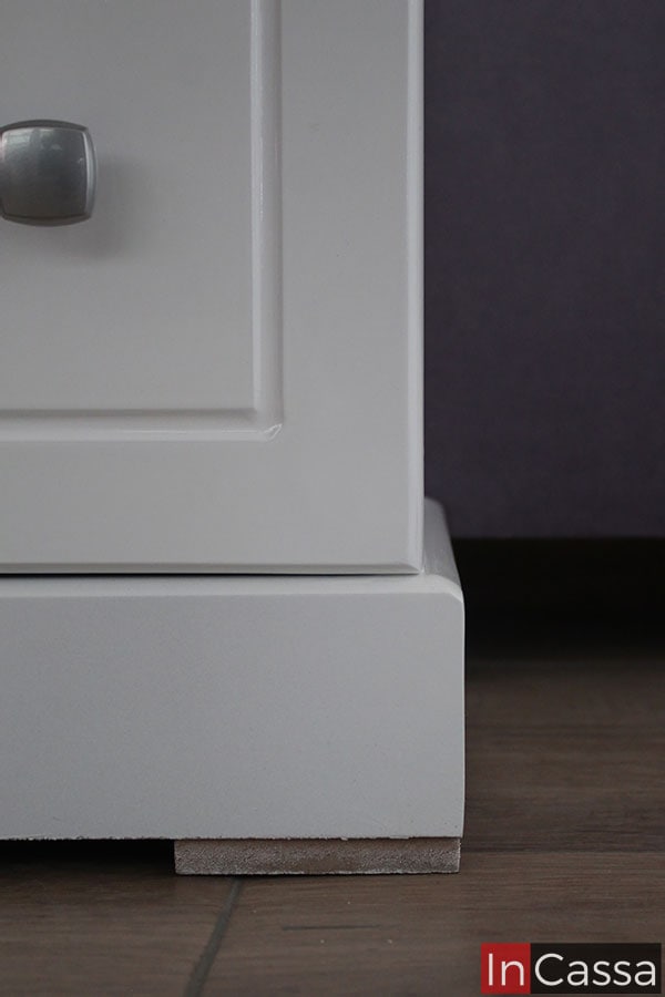 La toma se concentra completamente en la parte inferior de la cajonera infantil blanca, mostrando su gruesa base con amplias patas de madera.