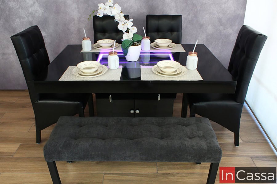 En esta toma se aprecia el comedor desde una perspectiva frontal, mostrando su diseño simétrico y la armonía entre la mesa negra, las sillas tapizadas en tacto piel negro y la banca de suede gris oxford. Este modelo combina comodidad y elegancia para complementar cualquier espacio.