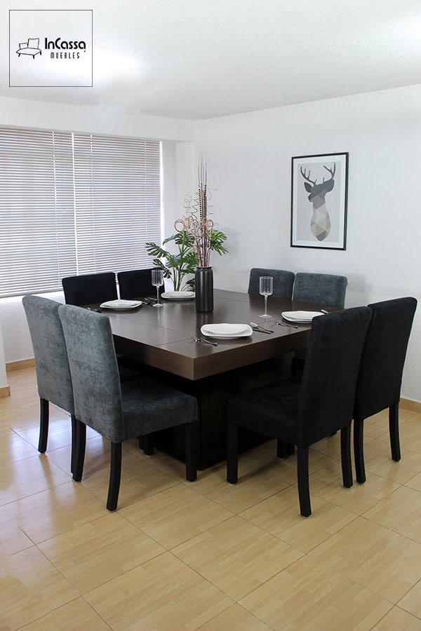 Comedor para 8 personas con 4 sillas tapizadas en suede gris y 4 sillas de suede negro, mientras que la mesa del comedor es de MDF chileno en acabado tabaco. EL comedor es presentado en una estancia con paredes blancas.