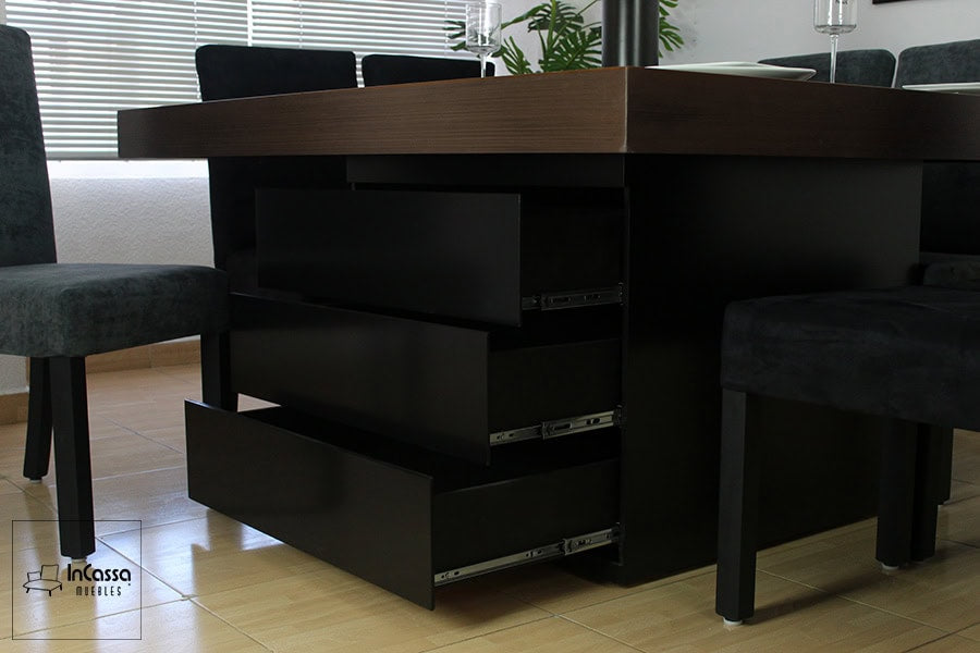 La toma se concentra en el pedestal del comedor de 8 sillas, el cual es de color chocolate y cuenta con 3 amplios cajones, cada uno con un sistema de rieles metálicos para su apertura y cierre.