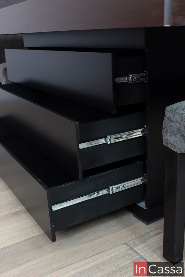 Se muestra una toma cercana del pedestal chocolate del comedor para 12 personas, el cuál es bastante amplio y cuenta con tres largos cajones integrados a sus estructura. Cada uno de los compartimentos cuenta con un sistema de rieles metálicos para su apertura y cierre.