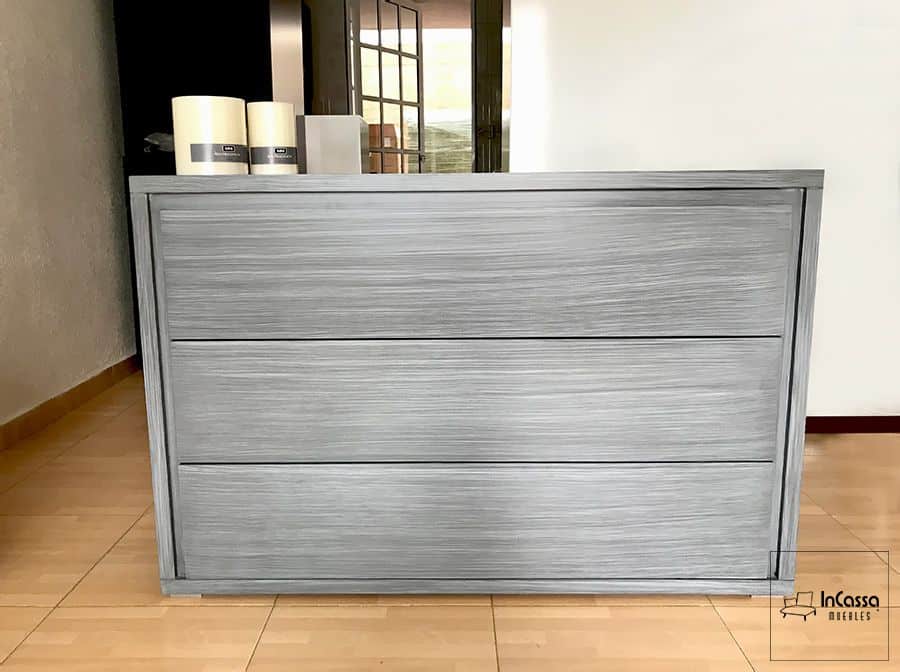 Se muestra un tocador de tres amplios cajones en tono gris cenizo oscuro con acabado texturizado, ideal para almacenar ropa y accesorios manteniendo la estética minimalista