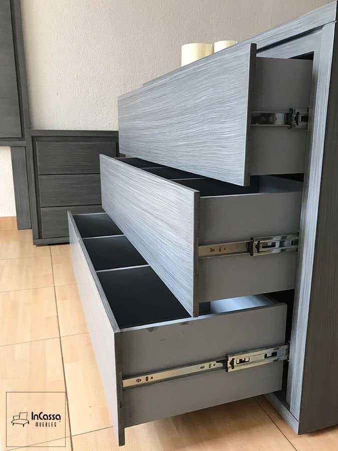 La toma resalta el tocador en acabado gris cenizo oscuro completo con sus cajones abiertos, equipados con correderas metálicas de extensión total, permitiendo un acceso fácil y un almacenamiento eficiente.