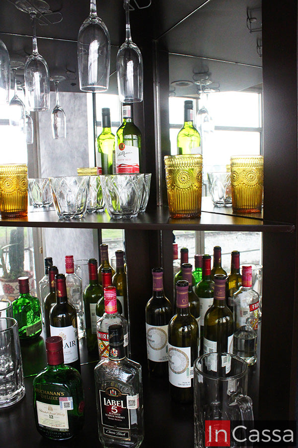 En primer plano, la Cantina Modelo LILIAN en acabado tabaco exhibe sus amplios compartimentos con fondo de espejo y colgadores para copas, ideales para organizar botellas y cristalería. Un diseño elegante que realza cualquier espacio dedicado a la convivencia y el entretenimiento.