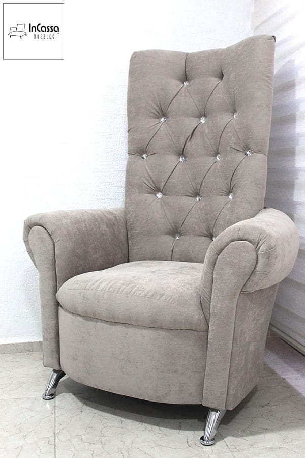 Este sillón tapizado en tela suede gris perla combina elegancia y confort. Su respaldo alto con capitoné y botones decorativos aporta un estilo clásico, mientras que los brazos curvos y las patas cromadas inclinadas le dan un toque sofisticado y moderno.