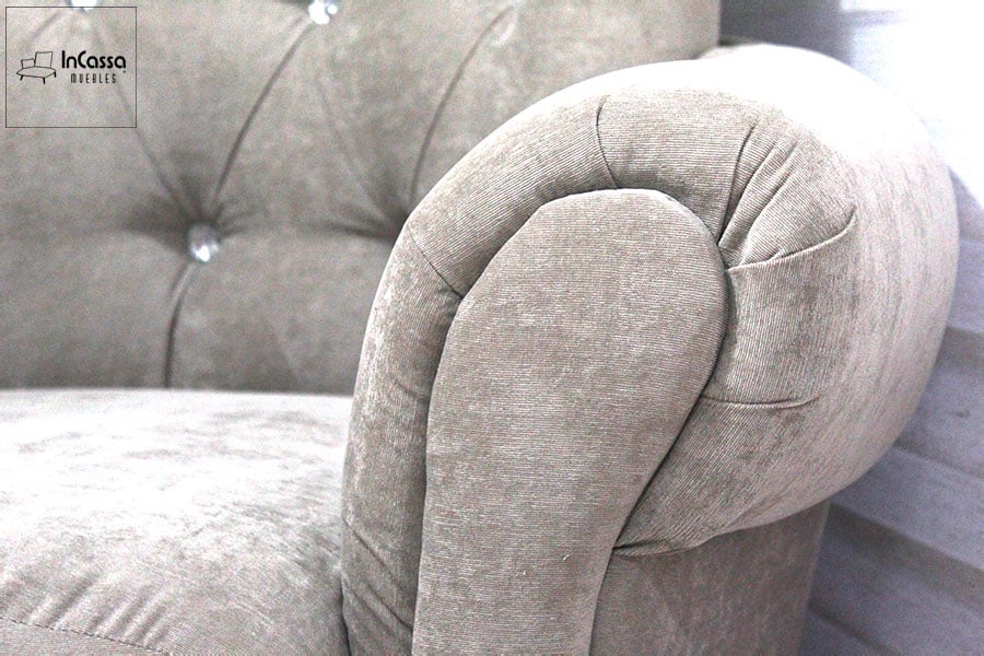 El diseño elegante de este sillón resalta con su brazo acolchado en forma curva, brindando comodidad y sofisticación. La textura de la tapicería suede en color gris perla, junto con el capitoné del respaldo, complementa su estilo clásico y refinado.