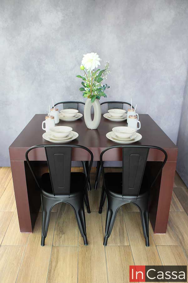 El comedor se muestra en una toma frontal, destacando su diseño robusto y limpio. La mesa de líneas rectas y el acabado tabaco con sillas metálicas negras reflejan una estética contemporánea que encaja en cualquier ambiente.