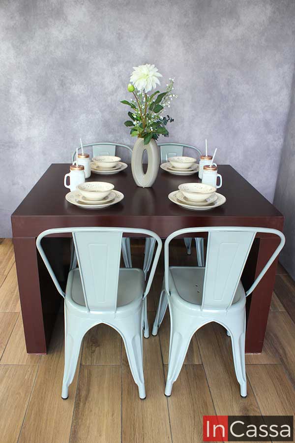 Dispuesto para una cena, el comedor tabaco con sillas metálicas grises, se muestra decorado con una vajilla sencilla que realza su aspecto moderno y funcional. El arreglo floral central añade un toque de frescura y estilo.