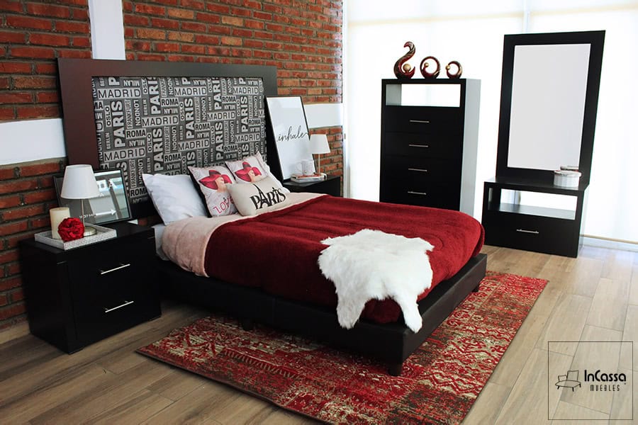 La imagen muestra la recámara moderna Lisbum con base color chocolate y cabecera tapizada en lino ciudades, acompañada de dos burós con tiradores metálicos. El juego incluye cómoda alta con cinco cajones y espejo con tocador, todo en acabado chocolate, sobre piso laminado y pared de ladrillo expuesto.