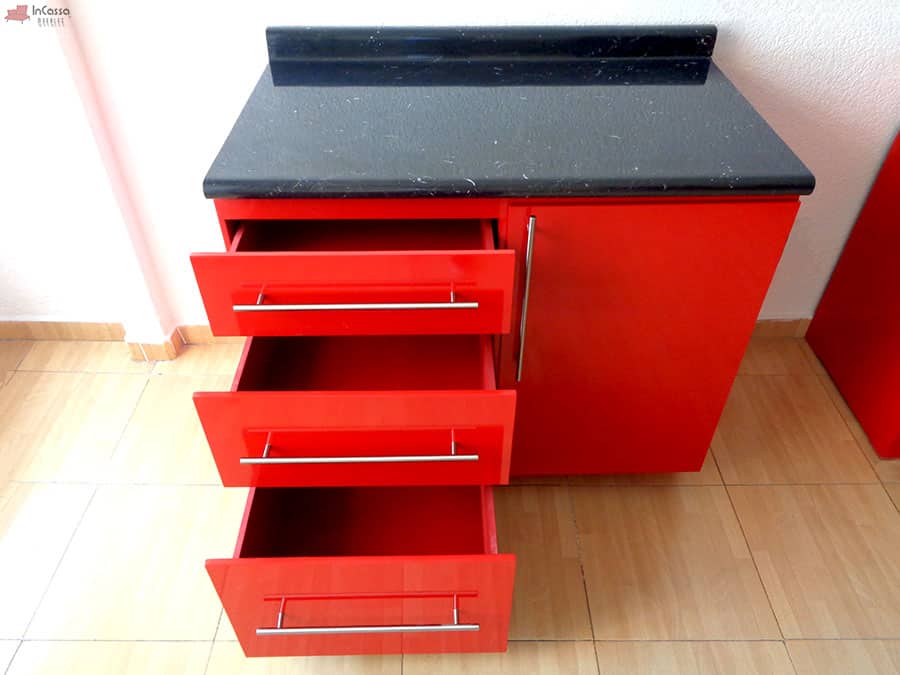 Una toma frontal del mueble carnicero rojo con cubierta de formica estilo mármol negro, en la que destacan los interiores de los cajones incorporados, en los que se conserva el color rojo. También tenemos una mejor vista de las jaladeras metálicas incluidas en los cajones y en la puerta.