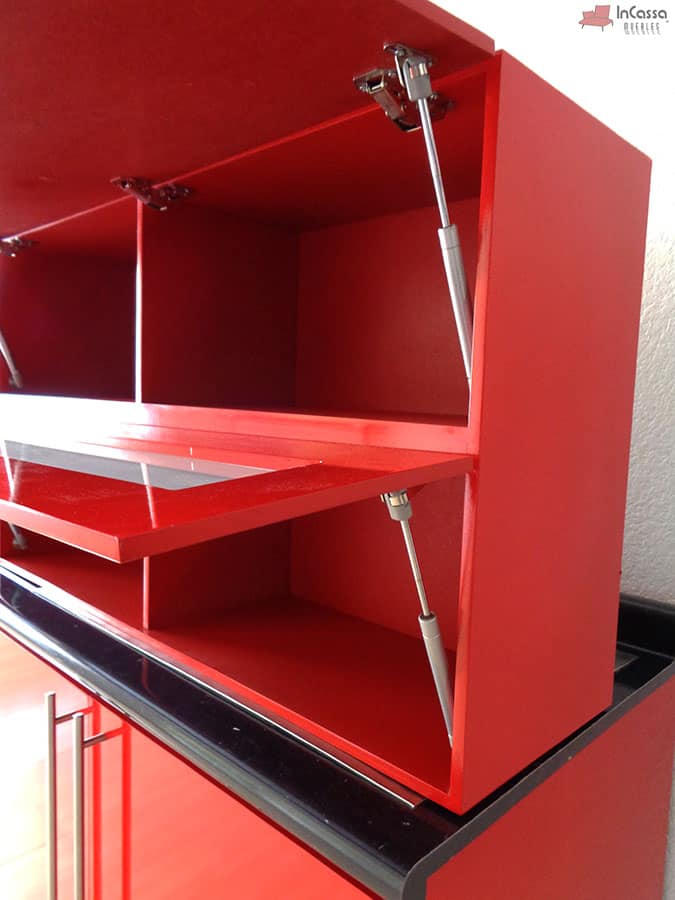 La foto nos enseña el interior de los módulos inferiores, en el que podemos ver que el color rojo está presente tanto en los exteriores como en los interiores del mueble. Además, también se nos muestran los pistones metálicos que permiten un sistema de apertura y cierre vertical a las puertas del módulo.