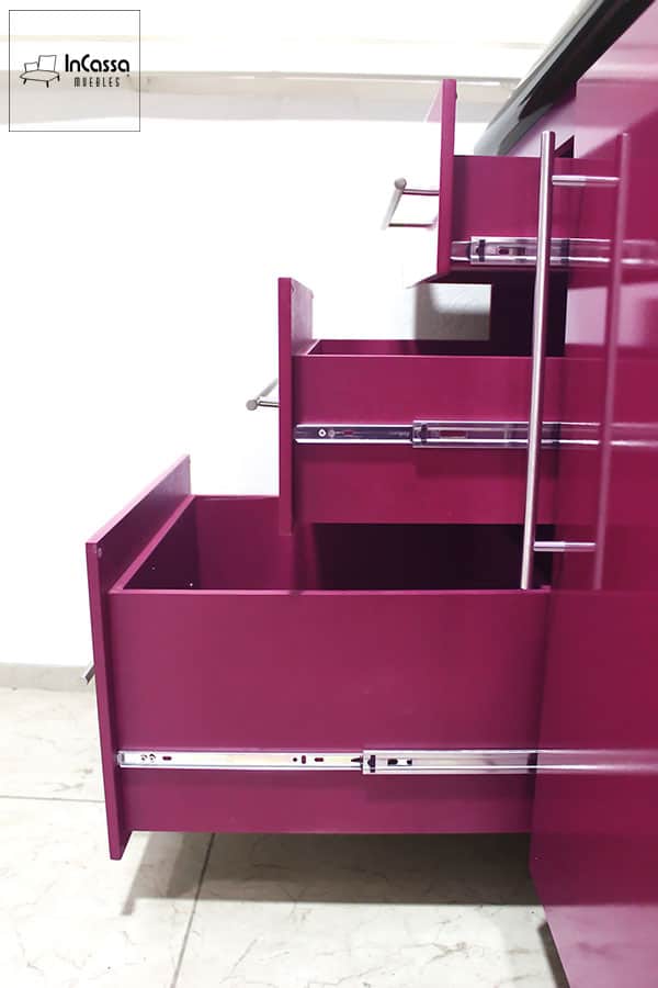 Toma lateral de los cajones integrados en el módulo inferior carnicero de la cocina. En la que podemos ver su estructura que conserva el color magenta presente en el resto de la cocina, además de los rieles metálicos que conforman el sistema de apertura y cierre de cada cajón.