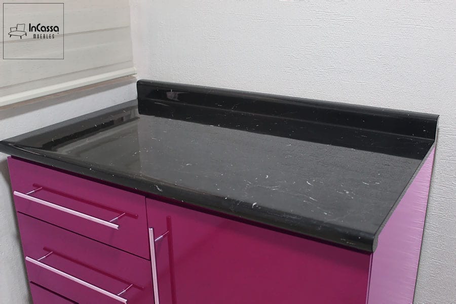 Una foto cercana a la cubierta del modulo inferior carnicero, la cual está fabricada de formica con estilo mármol negro. También podemos ver parte de los cajones, puerta y estructura del módulo, mismo que mantiene el mismo acabado magenta que el resto de la cocina.