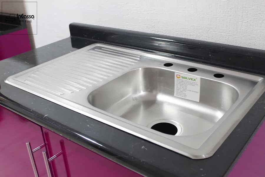 Imagen de la tarja de acero inoxidable con escurridor izquierdo incluida en la cocina magenta de 2.90m. Además podemos ver parte de la cubierta de la cocina, la cual es de formica estilo mármol negro.