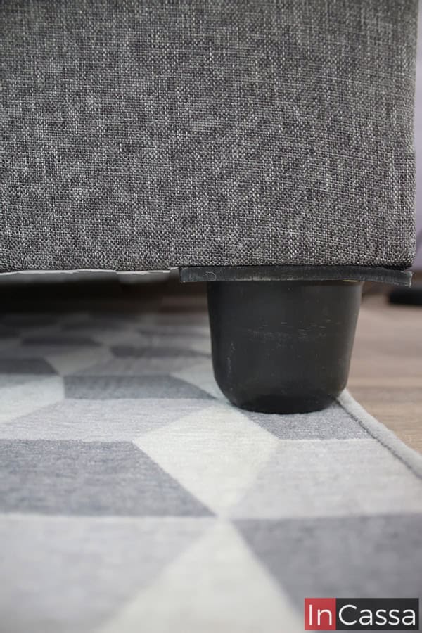 La toma se concentra en las patas del sofá-cama, las cuales son cuadradas de plástico en color negro. También se puede apreciar de manera más cercana la textura y acabado del tapizado lino mouse de la base del futon.