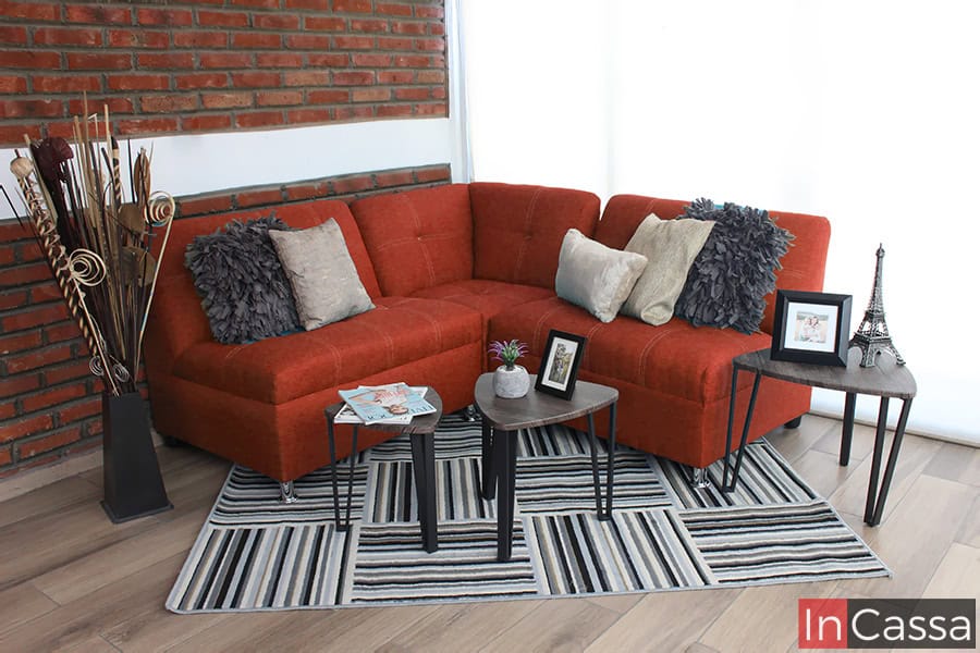 La imagen muestra la Sala Esquinera Modelo Londres tapizada en pliana color cobre, aportando calidez y un estilo contemporáneo. Sus cojines decorativos en tonos grises y beige generan contraste, mientras que la alfombra a rayas y las mesas auxiliares con base metálica completan un ambiente elegante y acogedor.